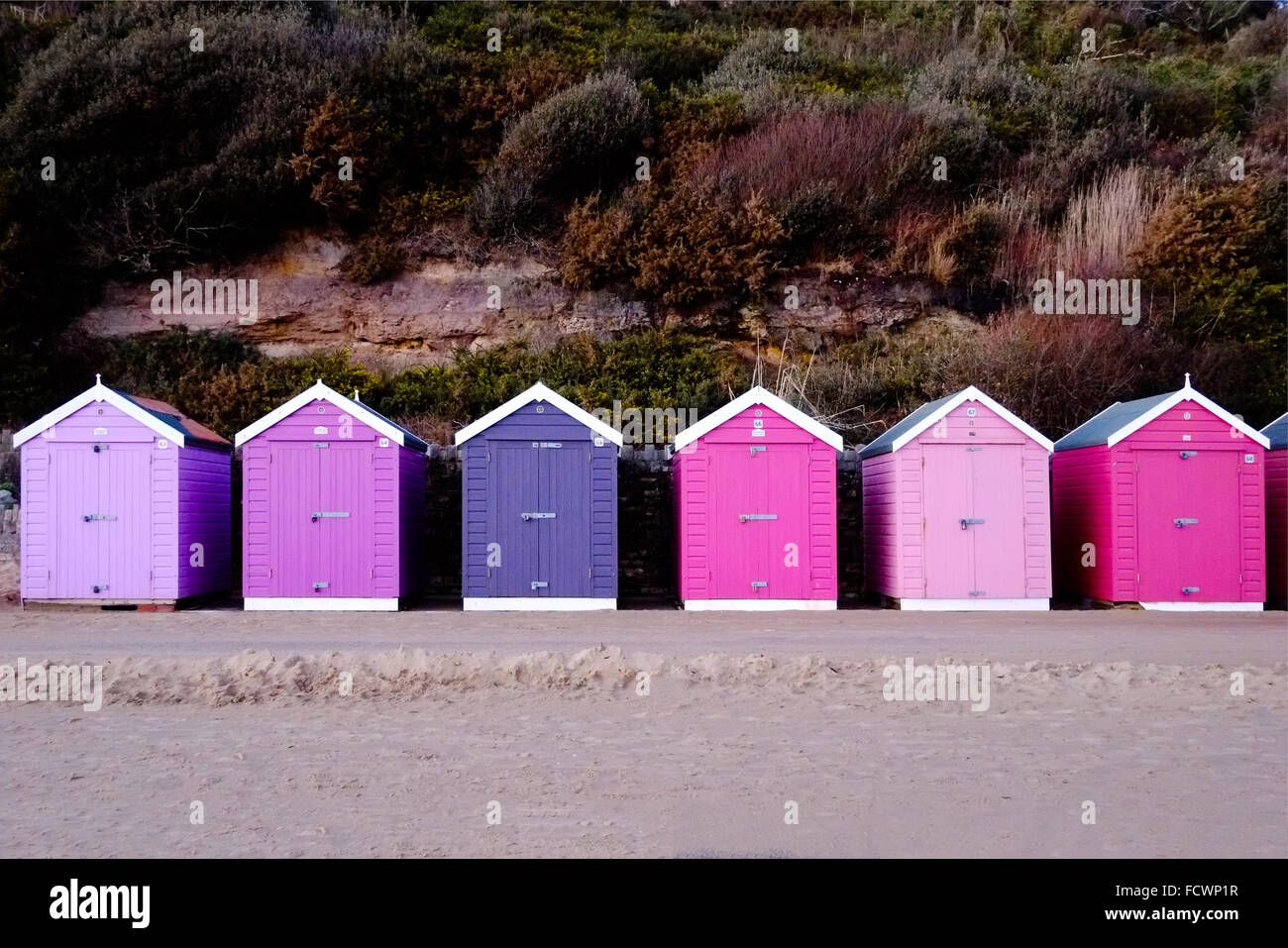 A row of brightly coloured beach huts on a sandy seafront in Bournemouth UK Stock Photo