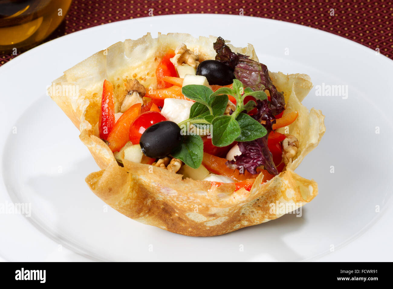 Vegetable salad with feta cheese, olives and nuts inside the pancake on white bowl Stock Photo