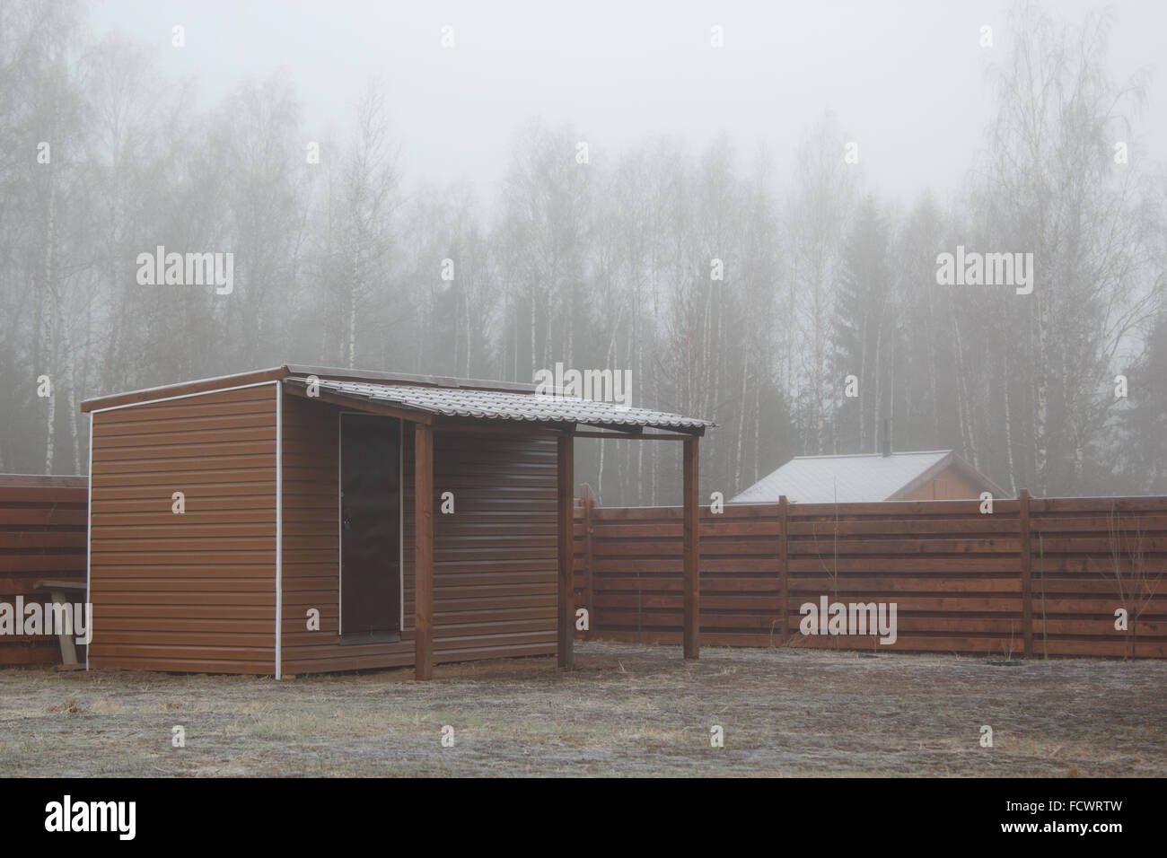 barn with a shed on frozen lawn in mist Stock Photo