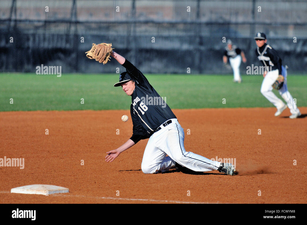 A high school third baseman working to secure a ground ball that had been headed down the left field line for a would-be double. USA. Stock Photo