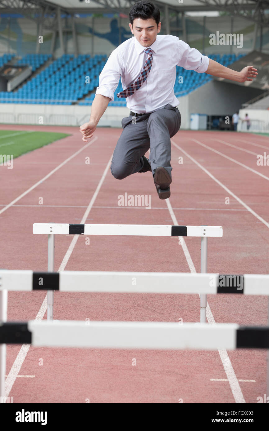 Man in business wear jumping over hurdles on a a track Stock Photo
