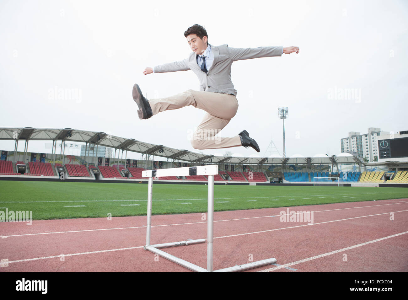 Man in business wear jumping over hurdles on a a track Stock Photo