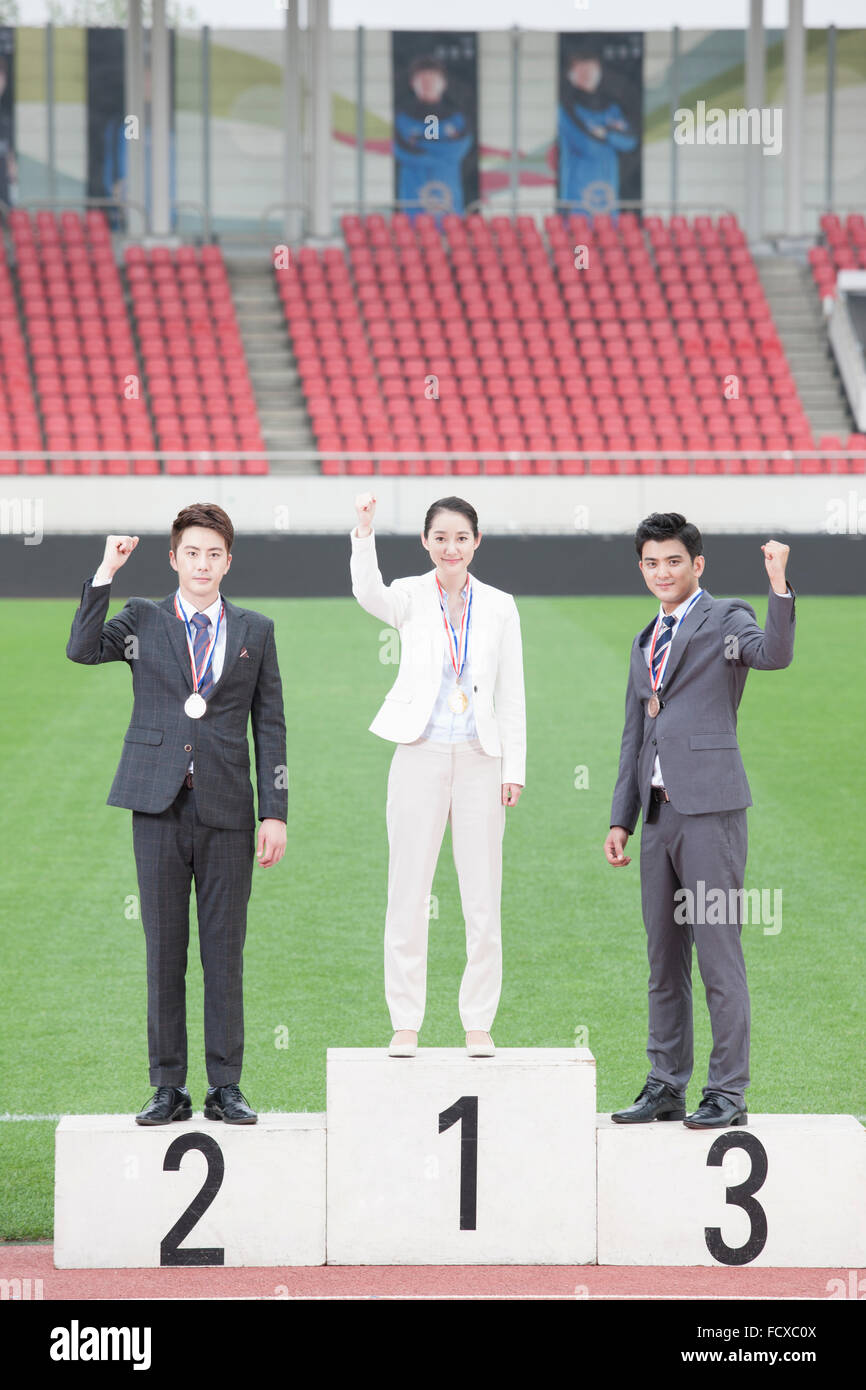 Business woman standing on the first place podium and two other business men standing on the second and third palace podiums Stock Photo