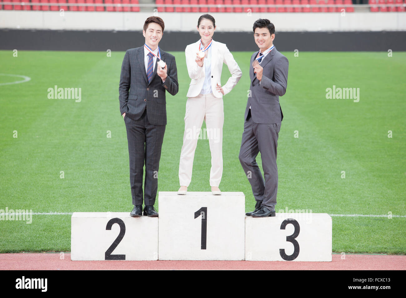 Business woman and two business men standing on winners podium and holding a medal each staring forward with a smile at sports Stock Photo
