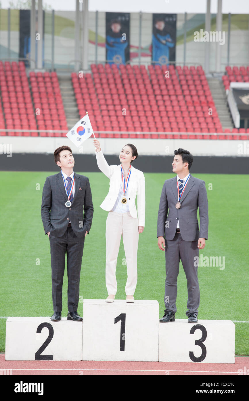 Business woman and two business men standing on winners podium and woman holding a Korean flag up Stock Photo