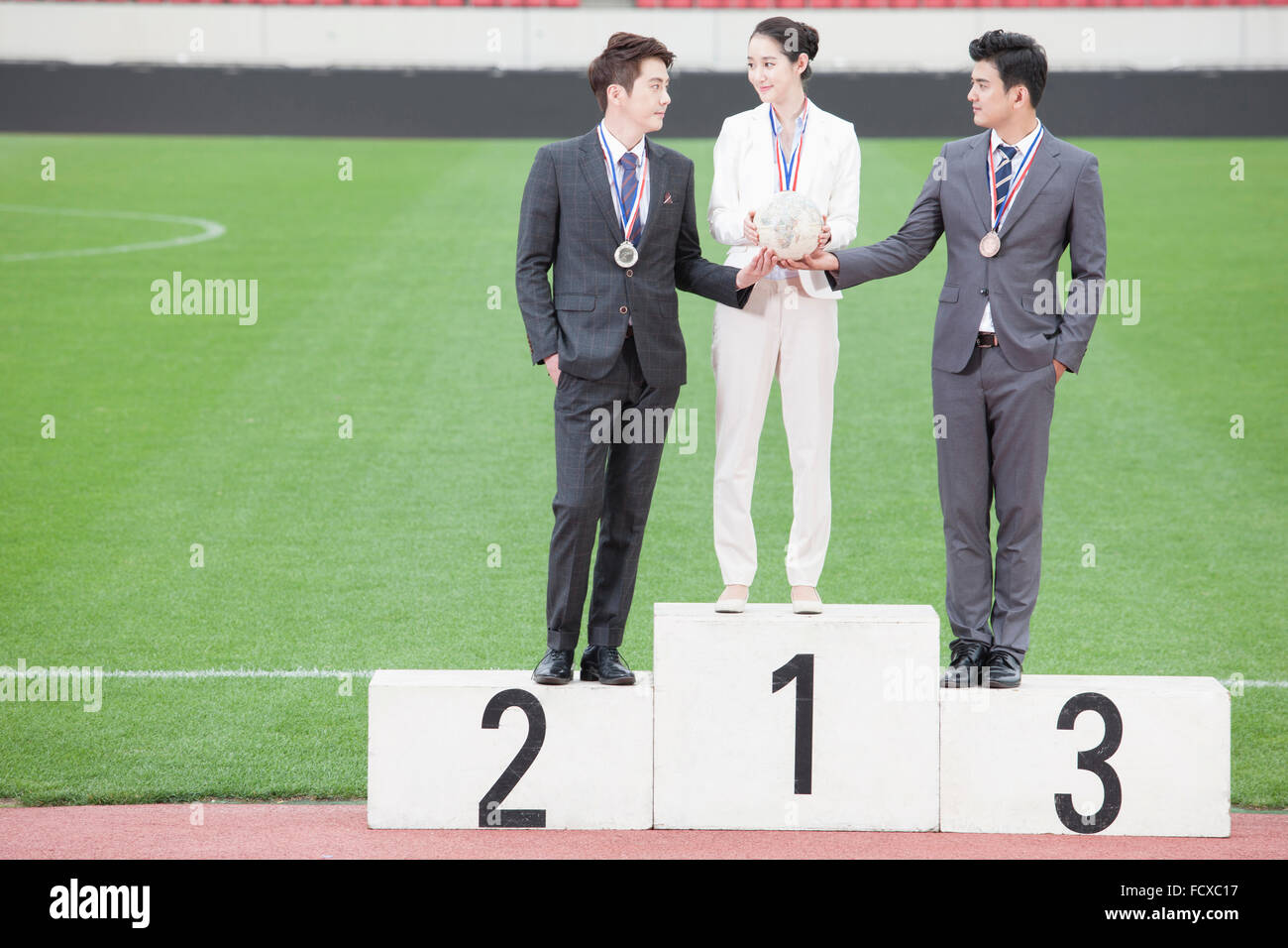 Business woman and two business men standing on winners podium holding a globe together and looking at each other at the sports Stock Photo