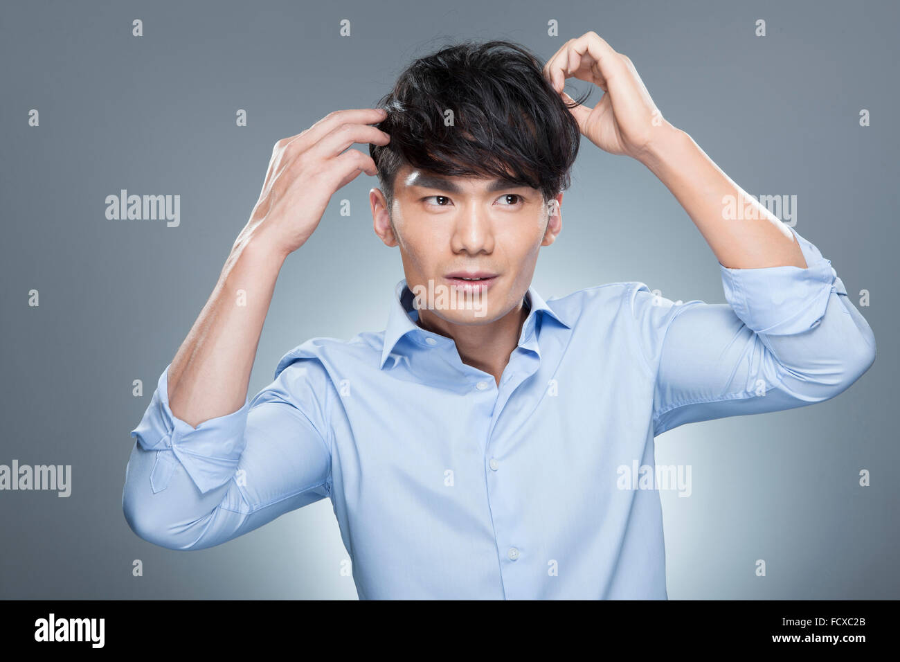 Man in blue shirt touching his hair and looking up Stock Photo