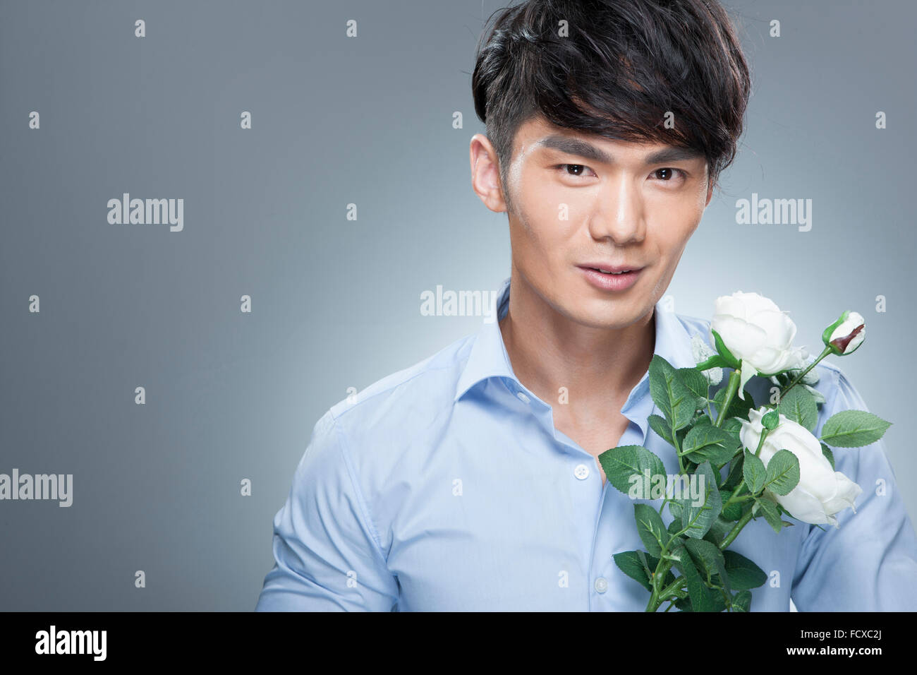Man in blue shirt holding white flowers and staring forward Stock Photo