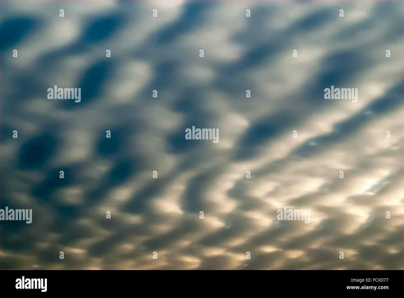 Abstract smooth gray and blue cloudscape with jagged wave forms and shadows, partly illuminated by sun behind clouds. Stock Photo