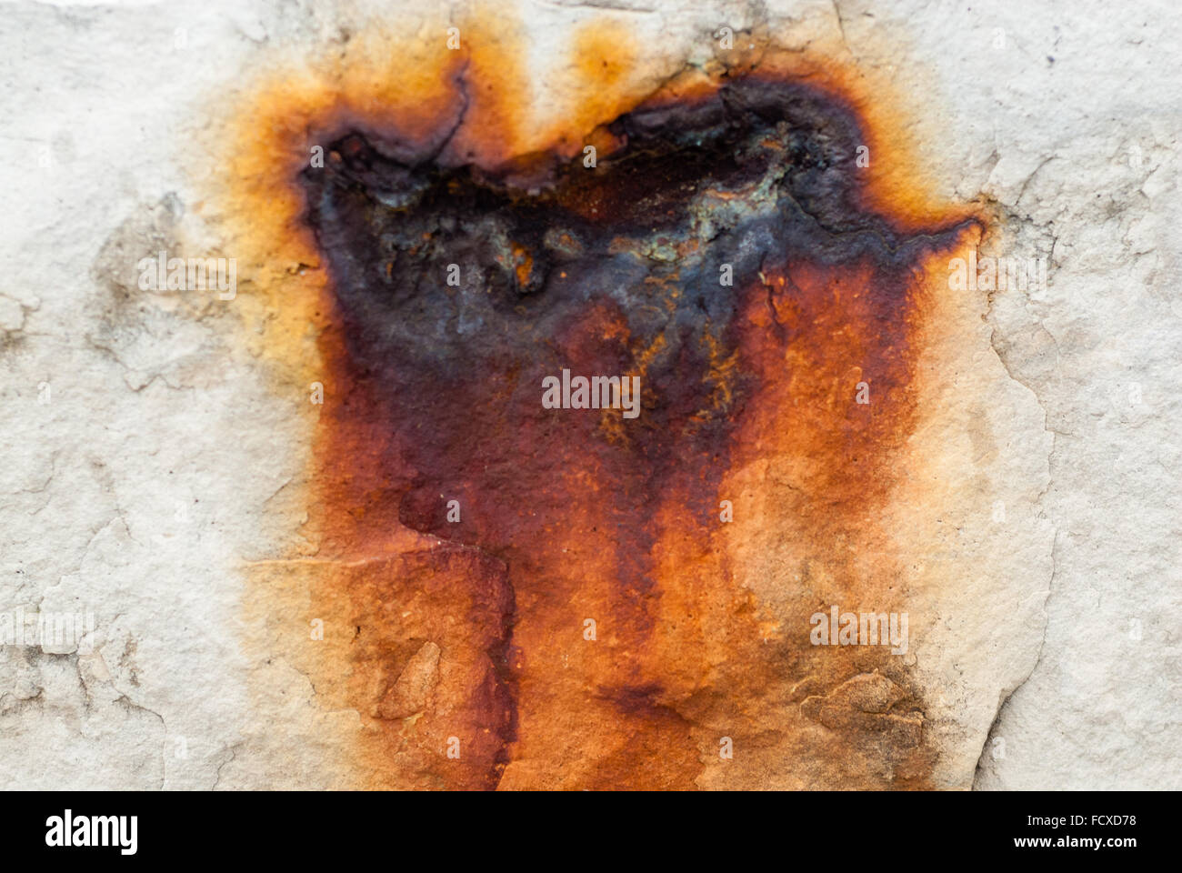 Rusted red burn scar on white stone wall, cracked and dripping with orange fringe. Stock Photo