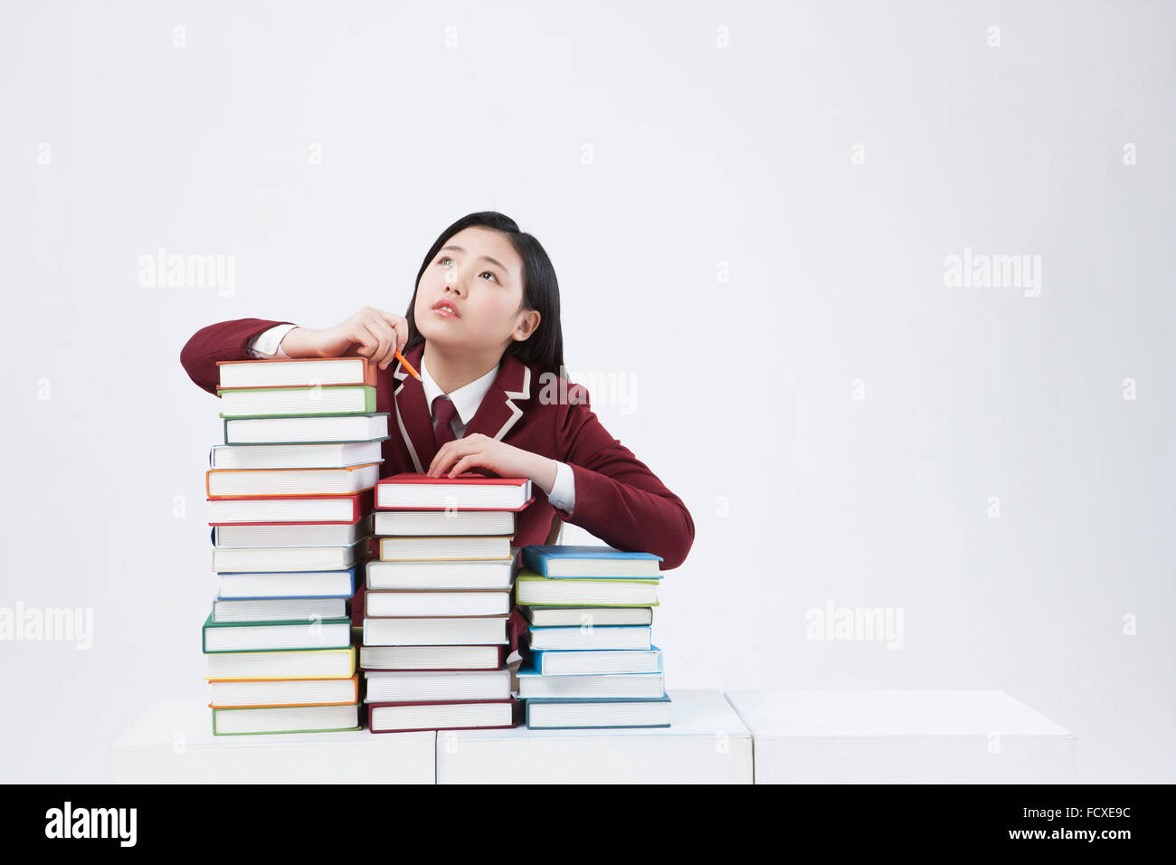 High school girl in school uniform leaning on piles of books and looking up in worried face Stock Photo