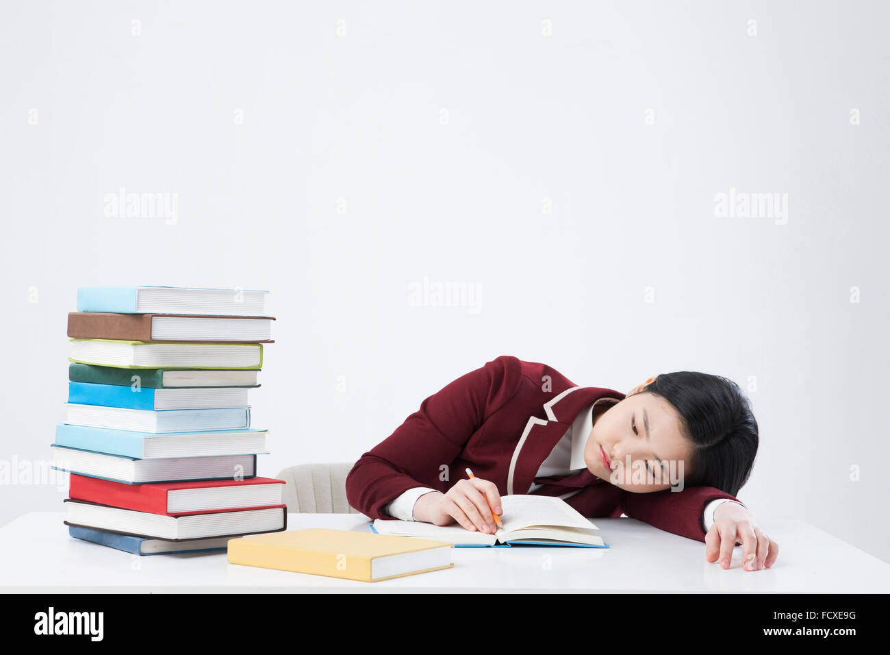 High school girl in school uniform putting her head on the desk with a pile of books on it in tiredness Stock Photo