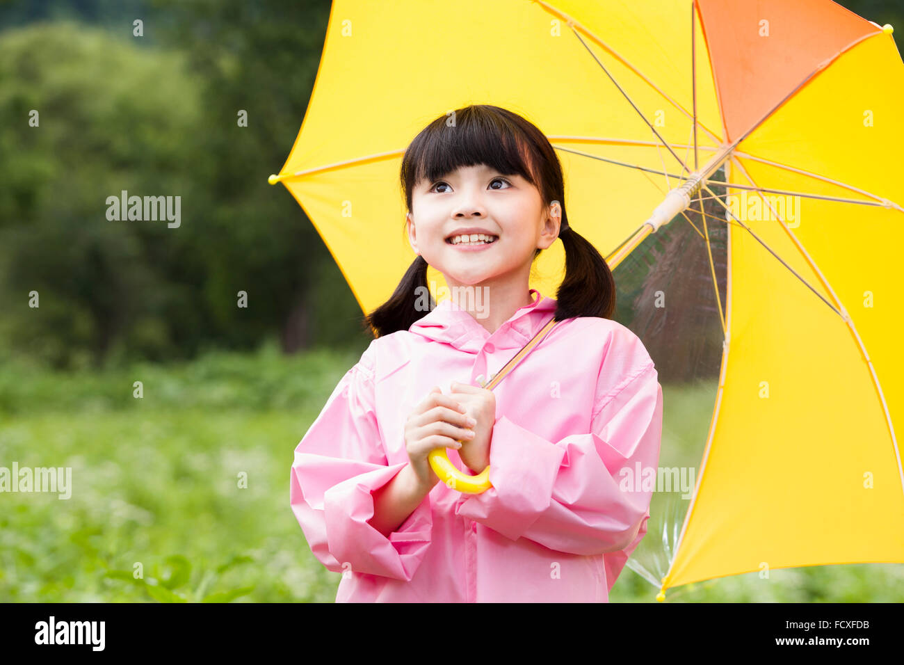 Girl in rain coat under an umbrella at field and looking up with a smile Stock Photo