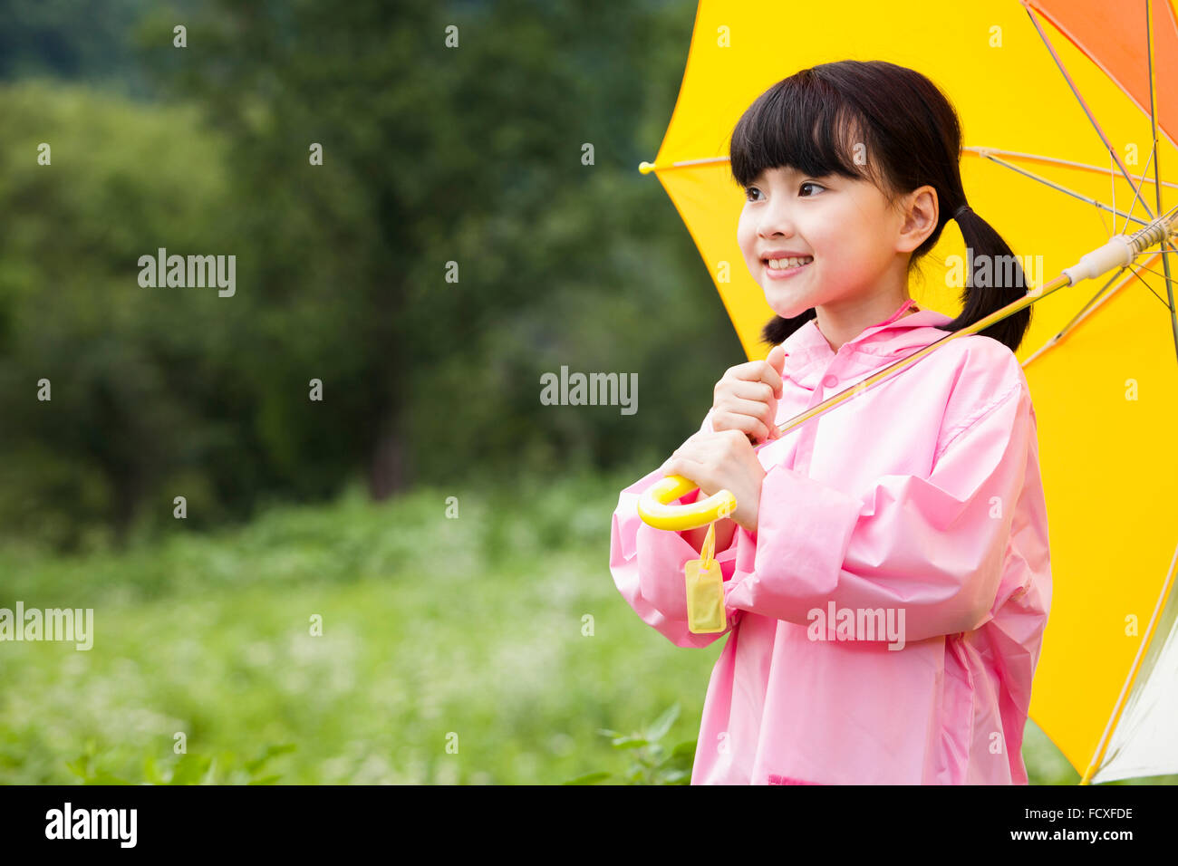 Girl in rain coat under an umbrella at field with a smile Stock Photo