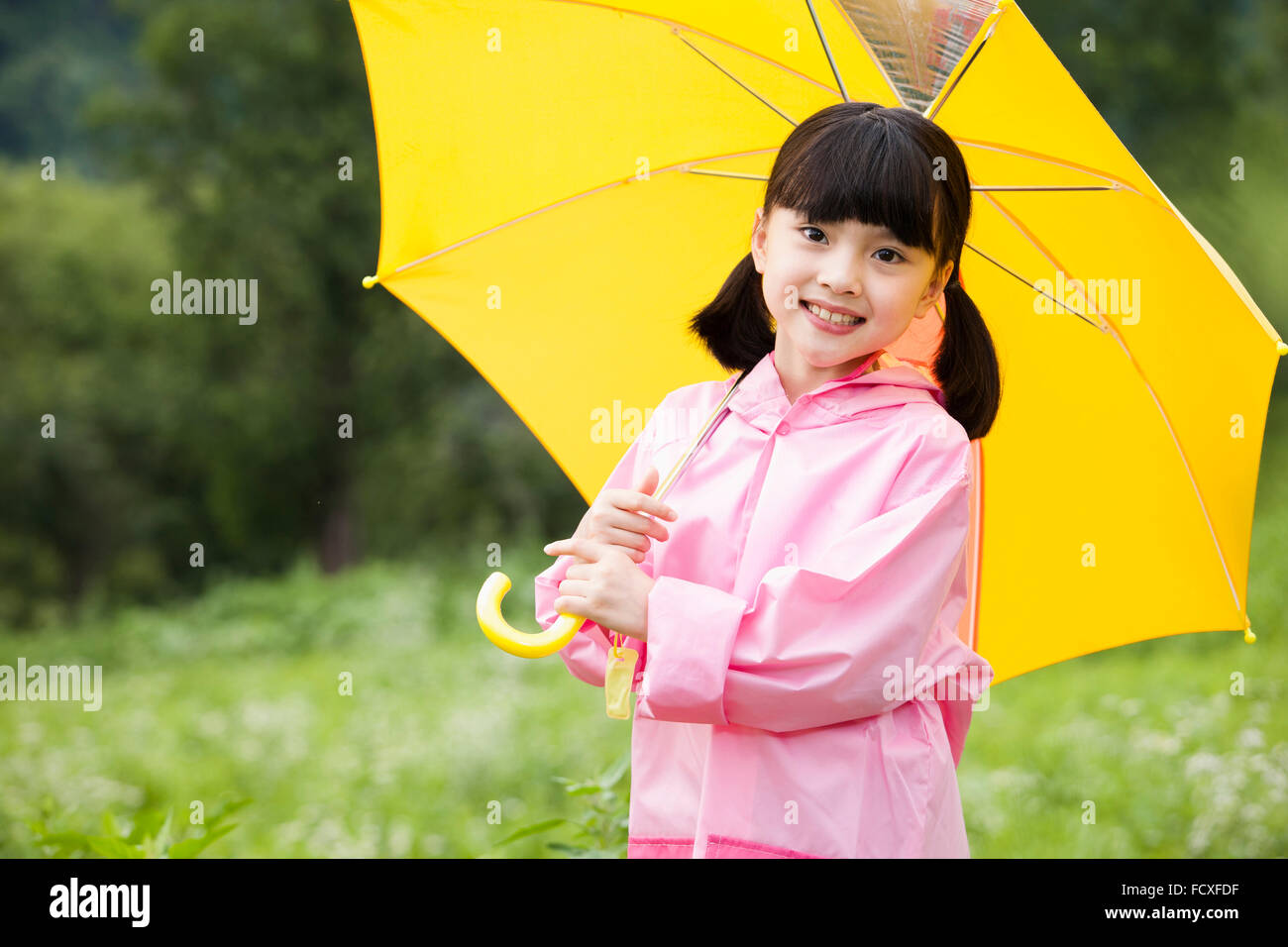 Girl in rain coat under an umbrella at field staring forward with a smile Stock Photo