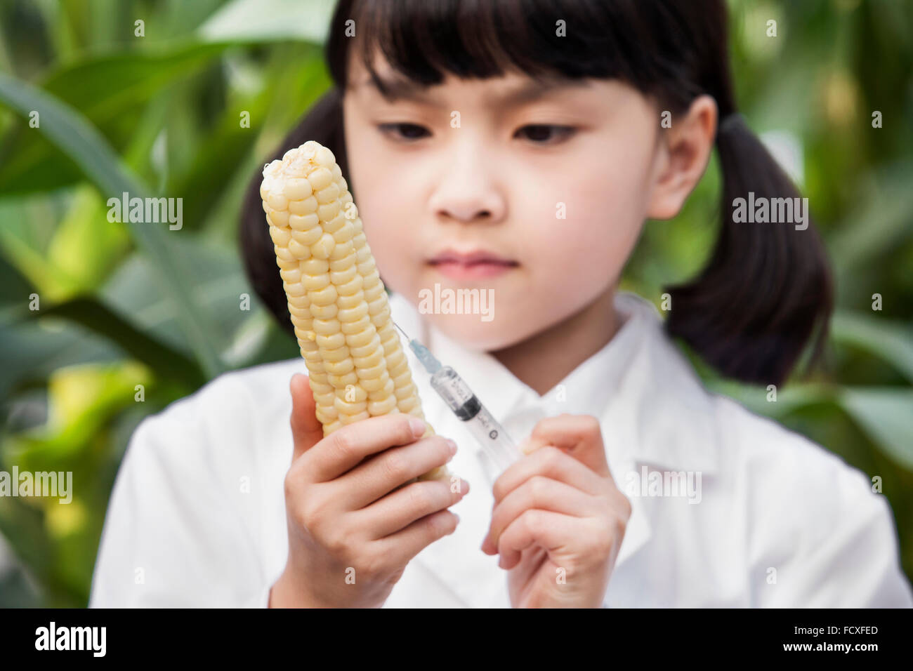 Girl in white gown putting a syringe on a corn in serious face Stock Photo