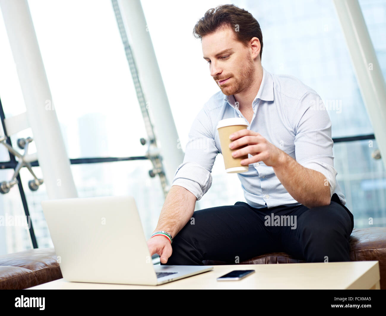 young business executive working on laptop computer hold a cup of coffee in modern office. Stock Photo