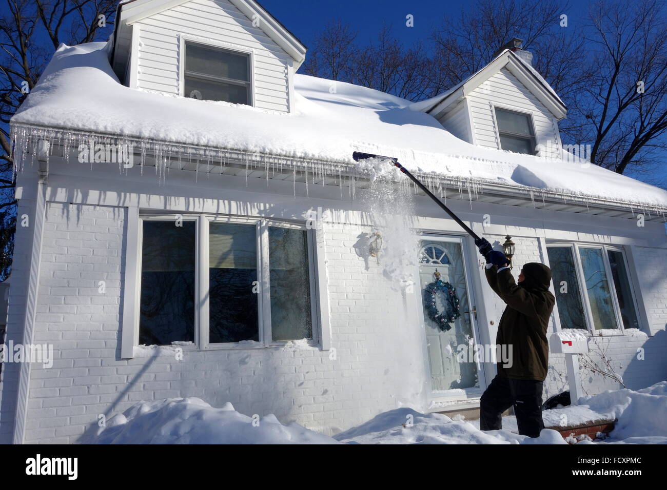 Homeowner using snow rake to clean snow and ice off of roof top after