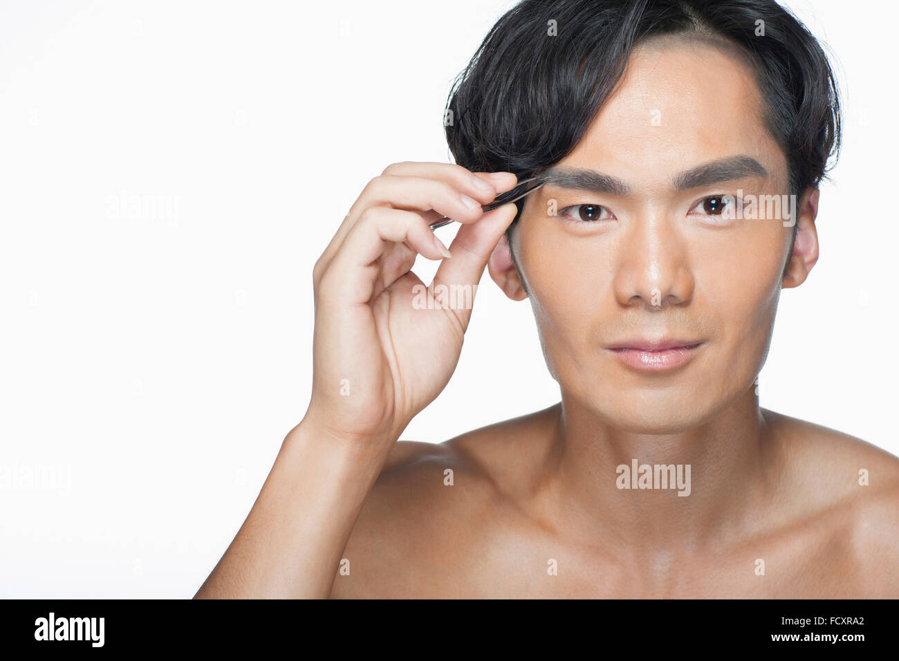 Portrait of young man tweezing eyebrow staring at front Stock Photo