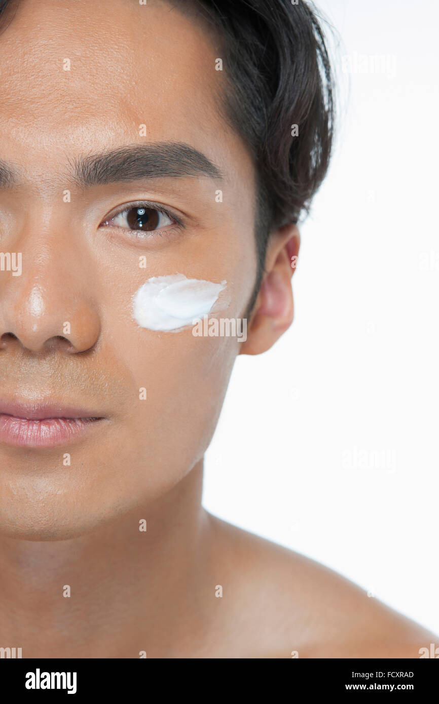 Portrait of young man applying lotion on his face Stock Photo