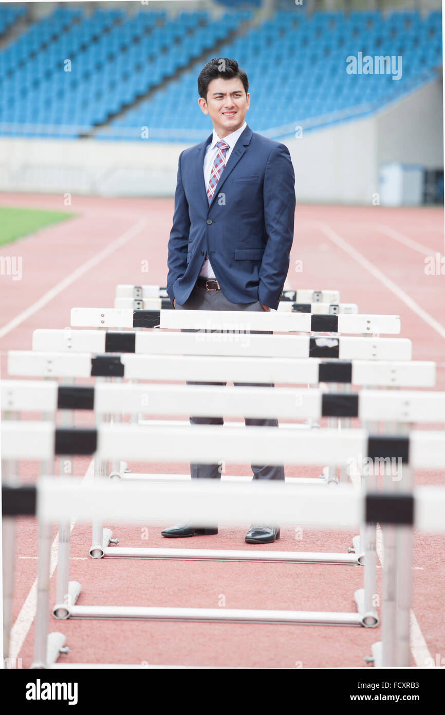Businessman standing at many hurdles on tracks at stadium Stock Photo