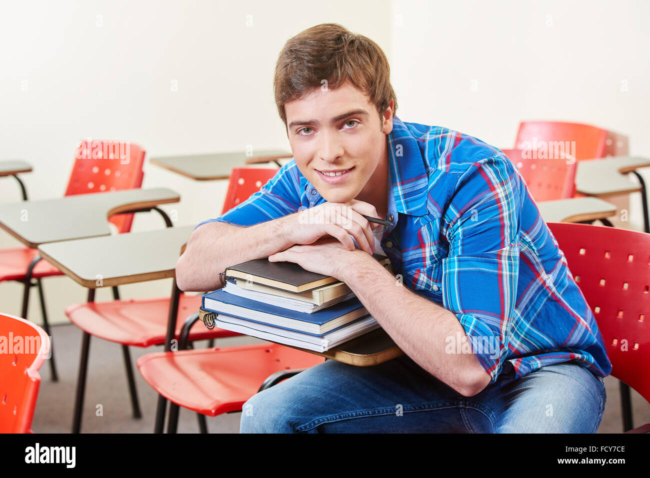 Smiling student leans on a stack of books in a classroom Stock Photo ...