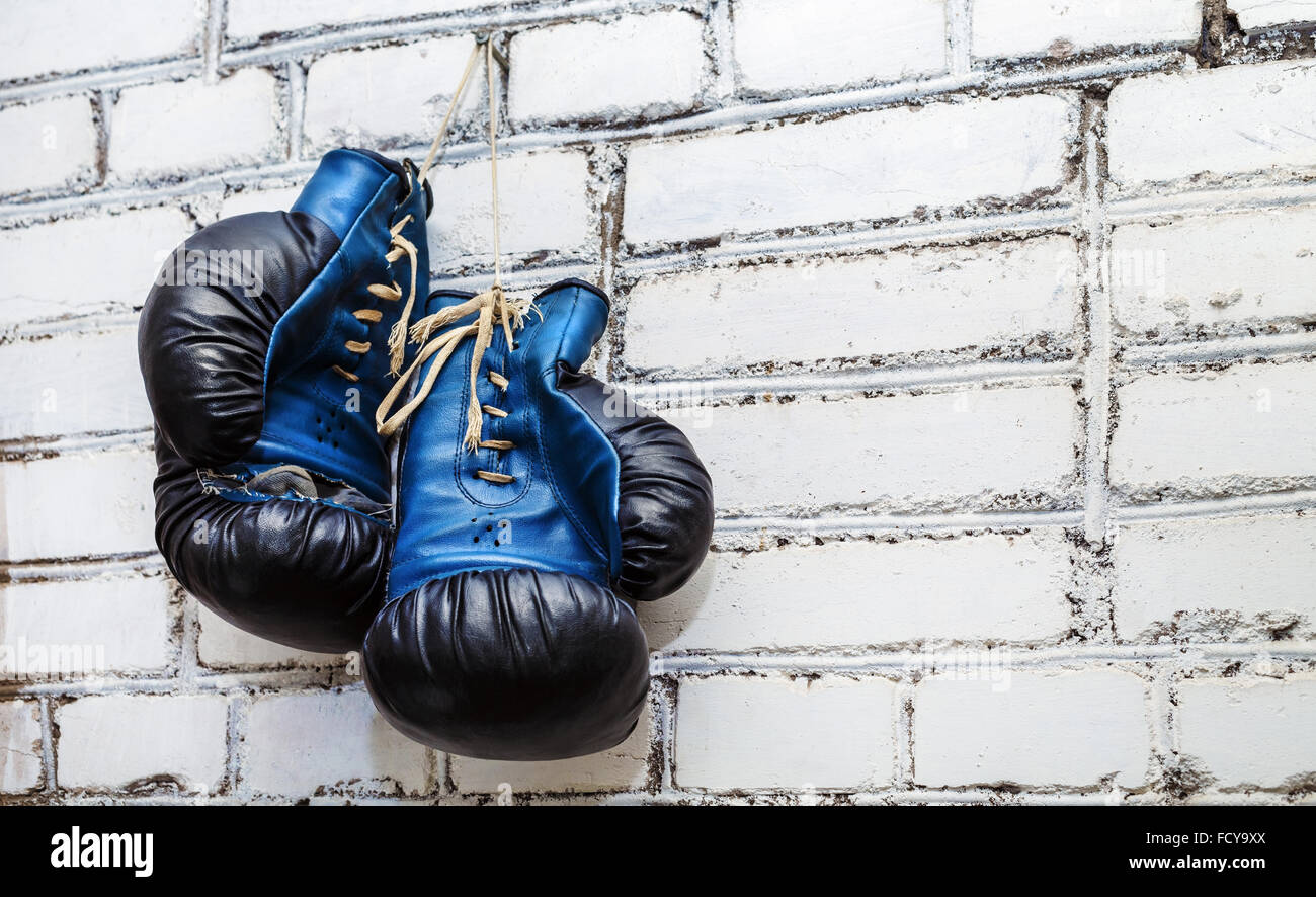 A pair of old blue and black boxing gloves hanging on white brick wall  background Stock Photo - Alamy