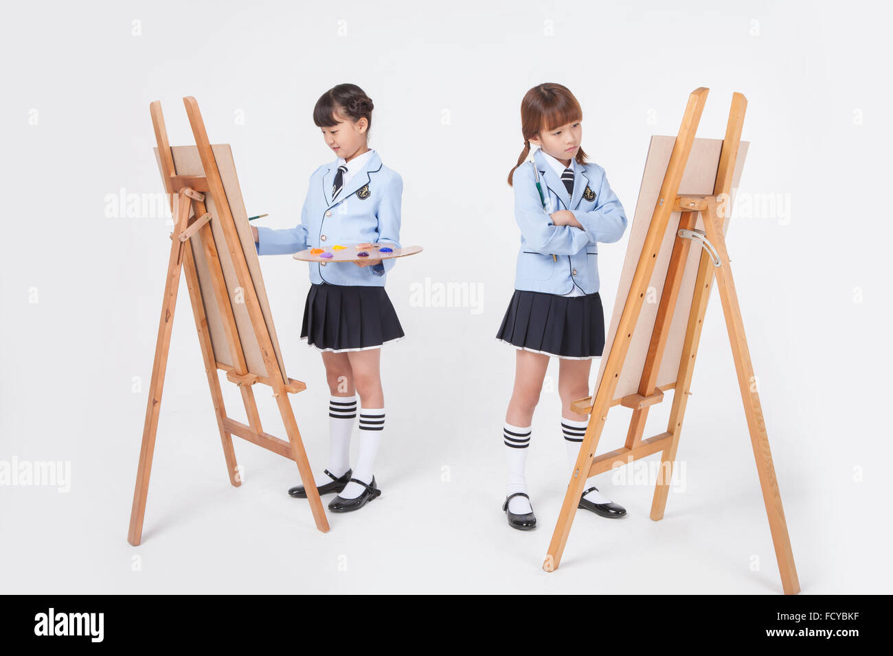 Two elementary school girls in school uniforms standing with an easel each and looking at it Stock Photo
