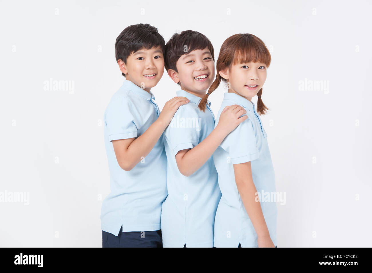 Three elementary school students in sportswear holding each other's shoulder and staring forward with a smile Stock Photo