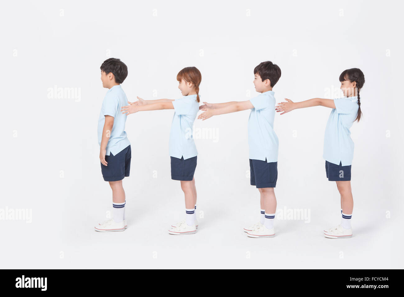 Four elementary school students in sportswear standing in line with their arms stretched forward Stock Photo