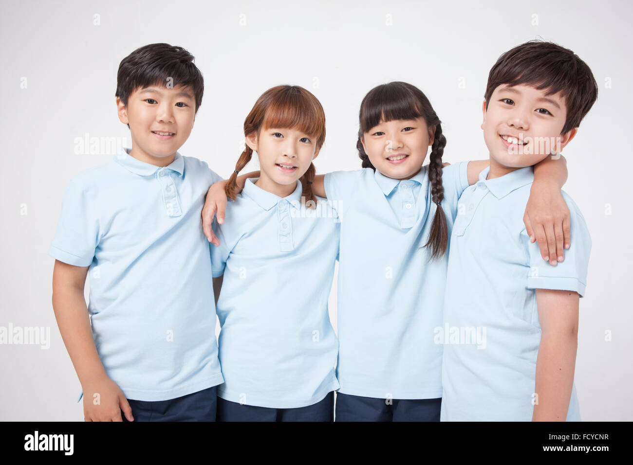 Four elementary school students in sportswear putting their arms around each other and staring forward with a smile Stock Photo
