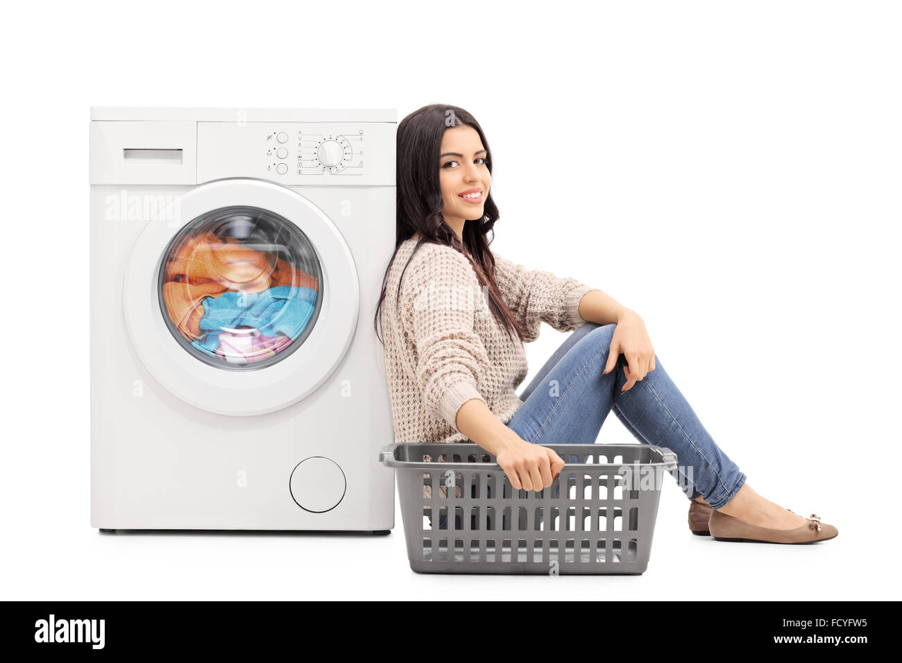 Young woman waiting for the laundry seated by a washing machine isolated on white background Stock Photo