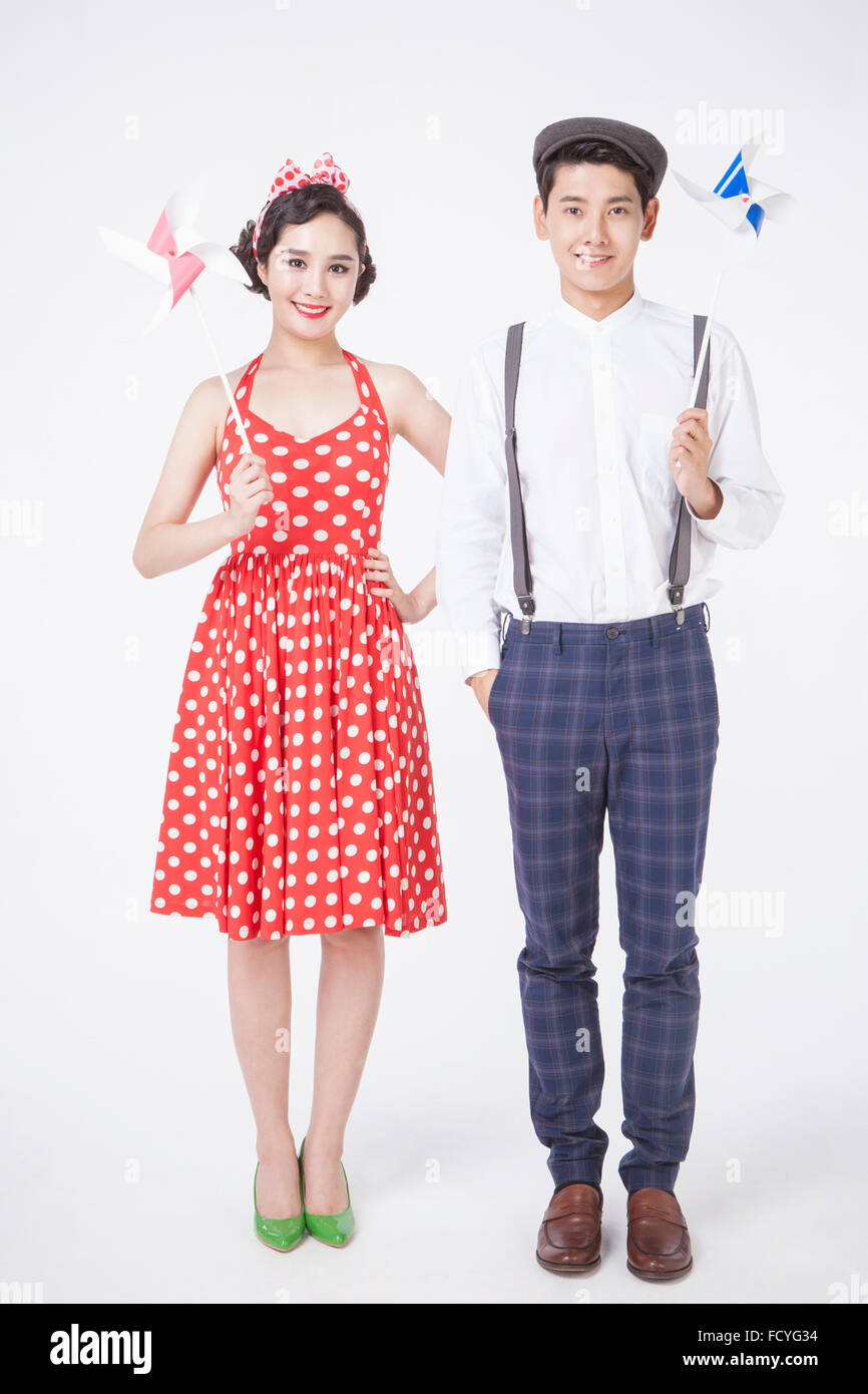 Couple in retro style fashion standing together and holding a pinwheel each both staring forward with a smile Stock Photo