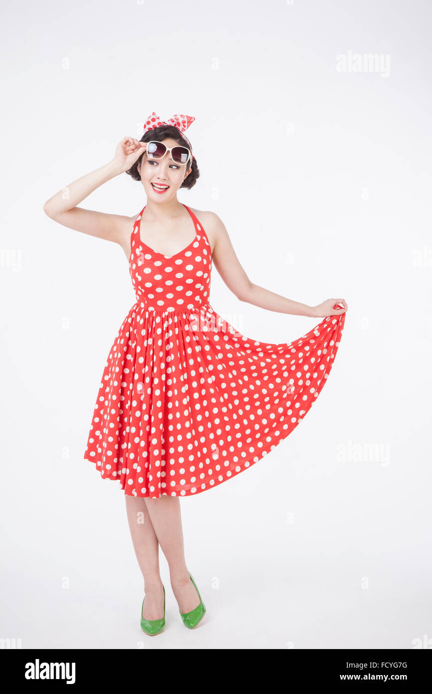 Woman in retro style dotted dress and sunglasses standing and holding her skirt and her sunglasses looking aside Stock Photo