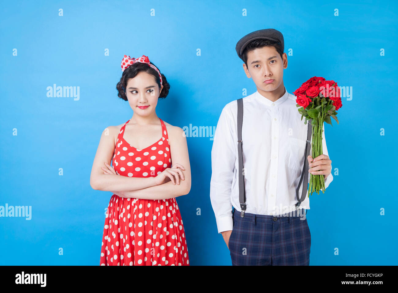 Man holding flowers and woman looking aside with her arms folded in angry face both in retro style fashion Stock Photo