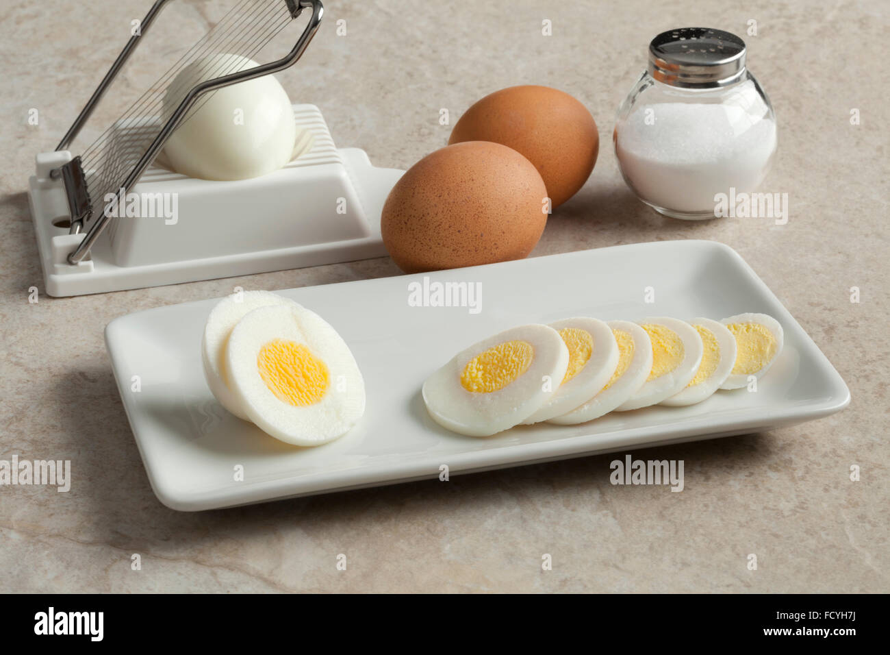 Hard boiled egg in slices on a dish with an egg slicer and salt on the background Stock Photo