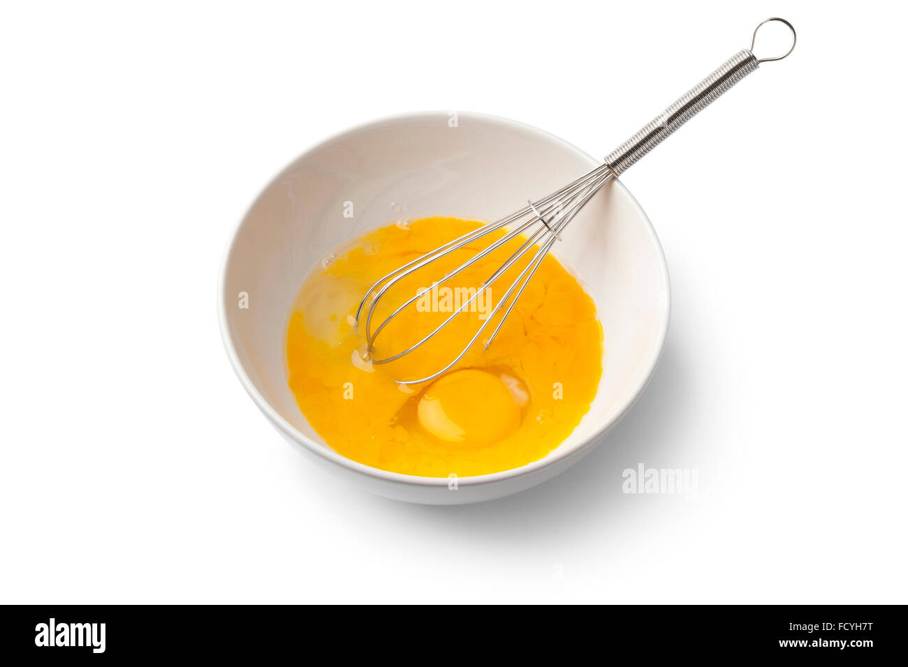 Beaten egg yolks in a bowl with whisk on white background Stock Photo