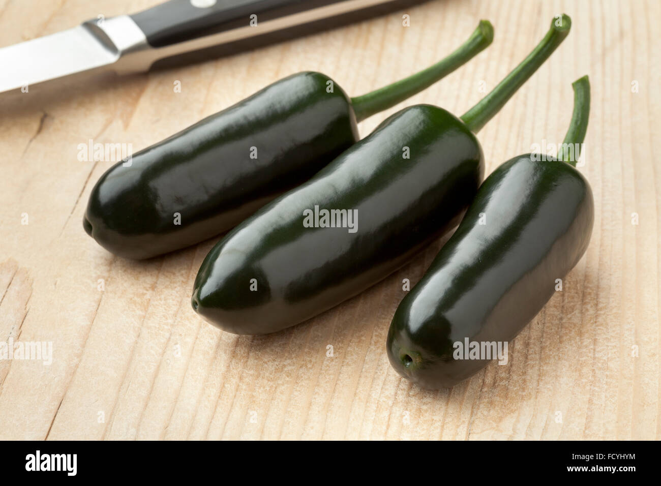 Three fresh green Jalapeno chili peppers on a cutting board Stock Photo