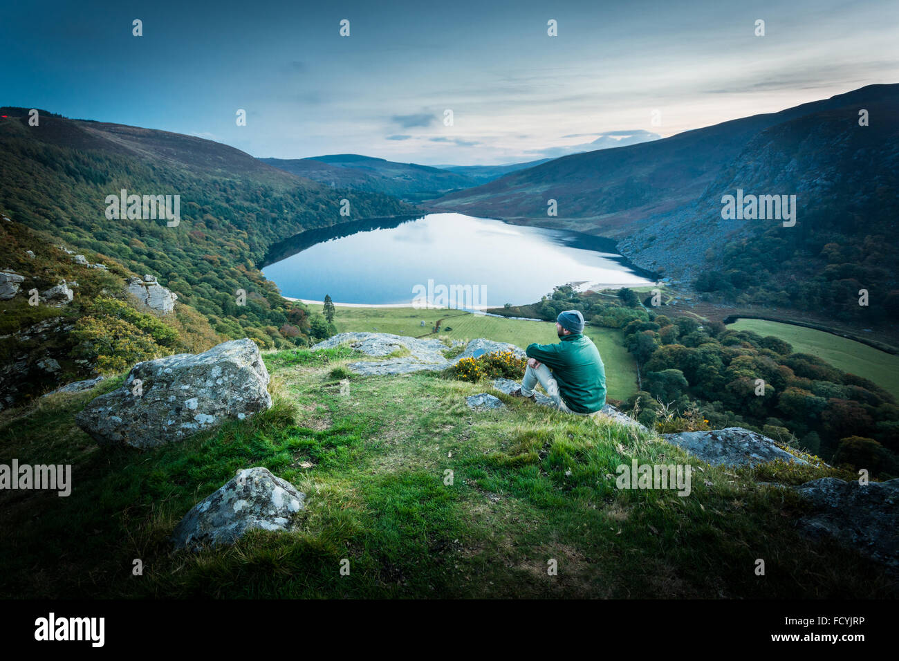 Hillwalker rests on a hill at dusk looking over the 'Guinness' lake Lough Tay and Luggala in county Wicklow, Ireland Stock Photo