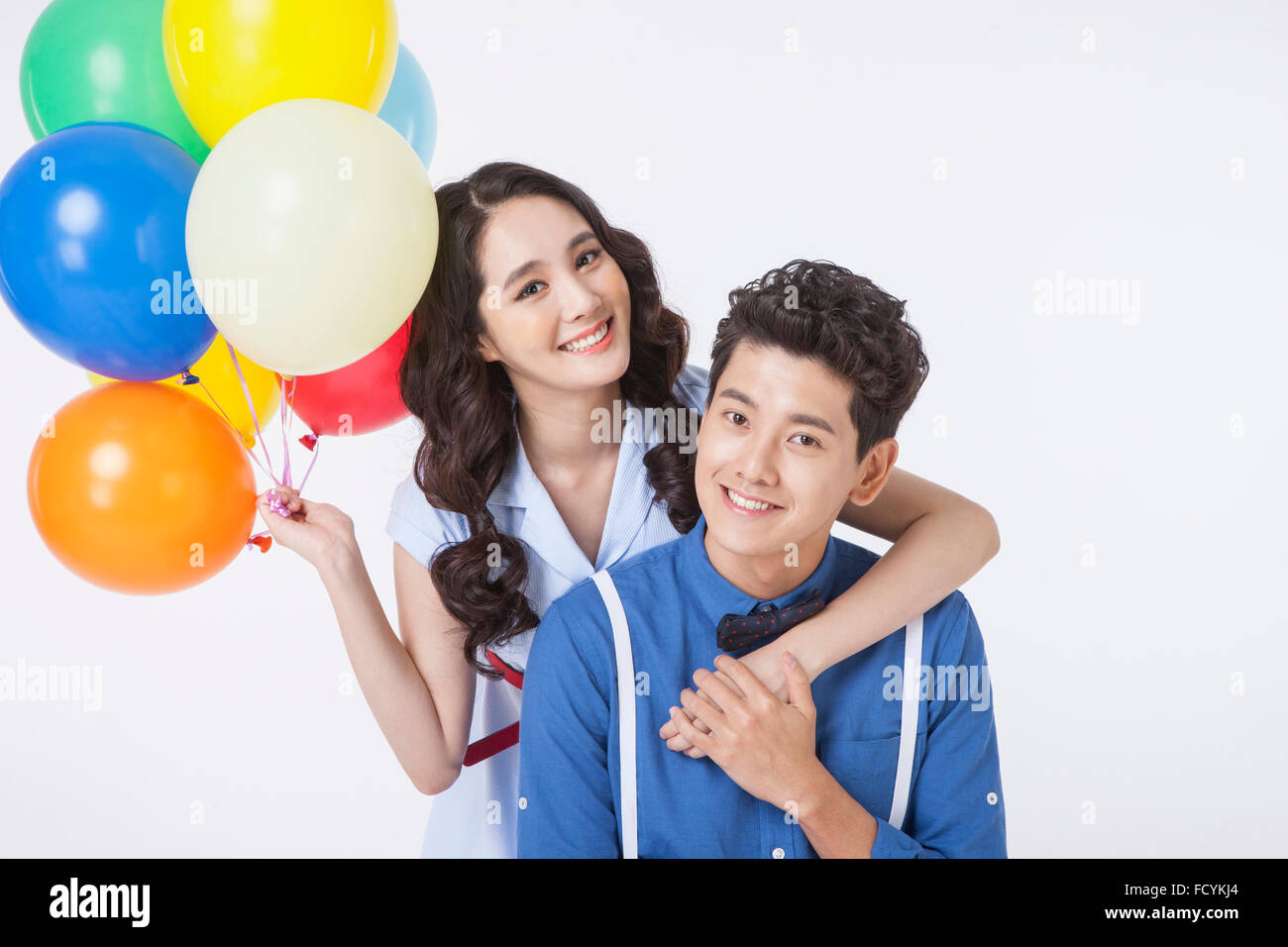 Woman with colorful balloons hugging from behind a man and both staring ...