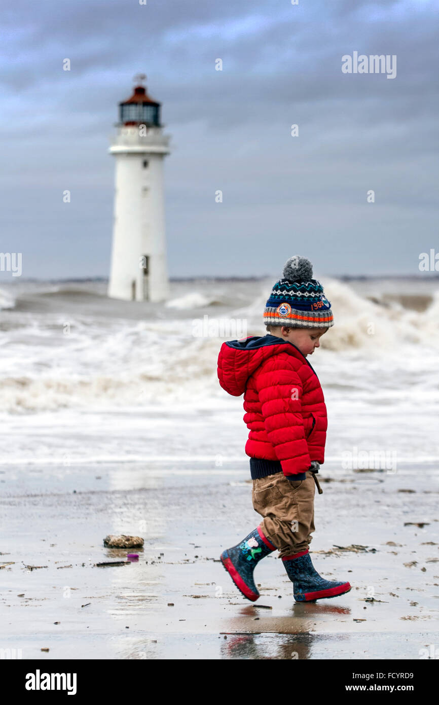 Young boy walks on the beach in stormy weather at New Brighton, Birkenhead, Liverpool, UK. 26th January 2016. UK winter weather. High waves crash Fort Perch Lighthouse and against the sea defences at Birkenhead, The Wirral, UK Stock Photo