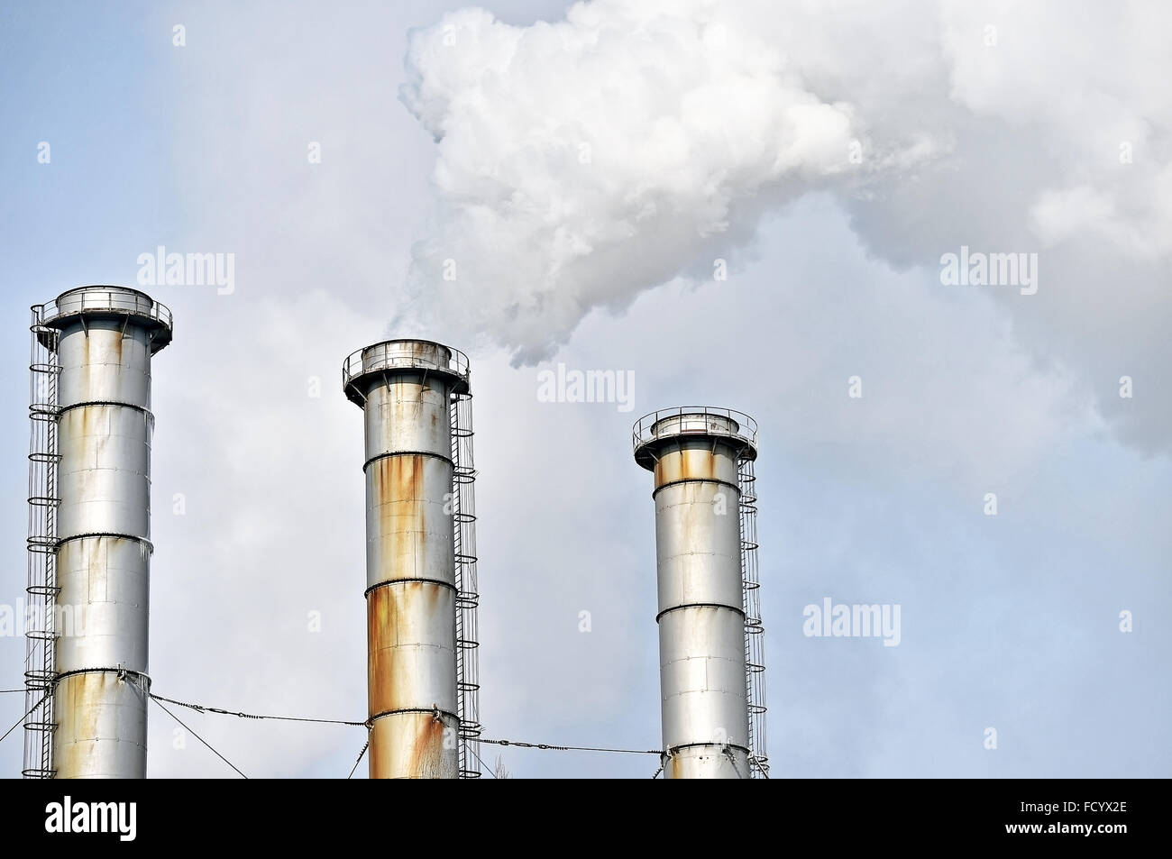 Smoke and steam coming out from an industrial petrochemical plant chimney with a blue sky on the background Stock Photo