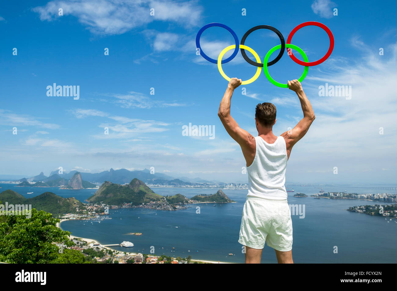RIO DE JANEIRO - OCTOBER 24, 2015: Athlete holds Olympic rings under bright blue sky above the city skyline. Stock Photo