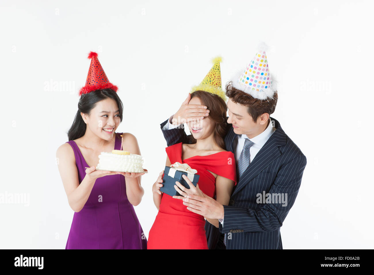 Three young adults celebrating the woman's birthday with a cake and a gift all in party hat Stock Photo