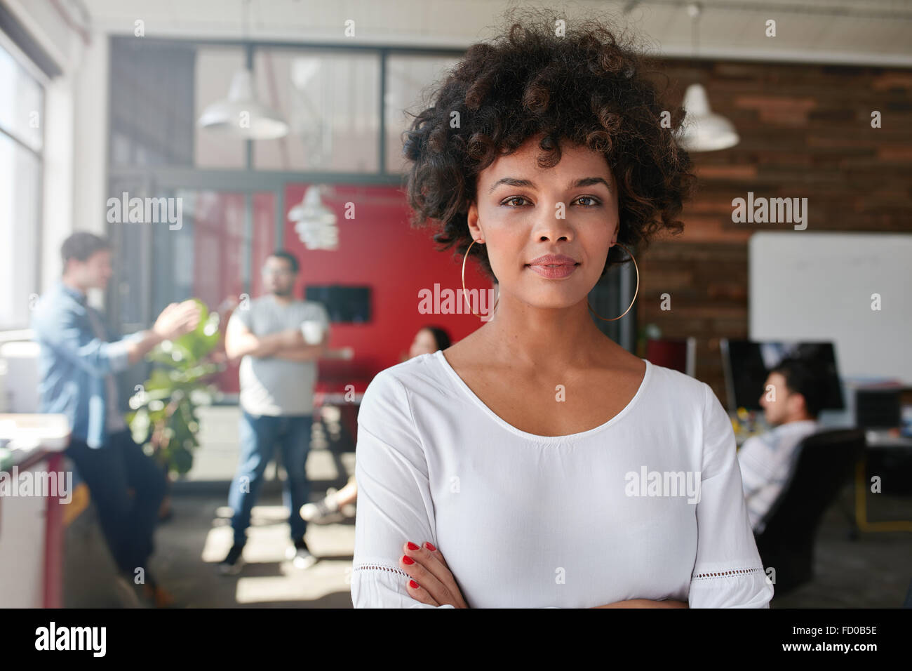 Portrait of woman standing in busy creative office looking at camera. Attractive female creative professional in design studio. Stock Photo