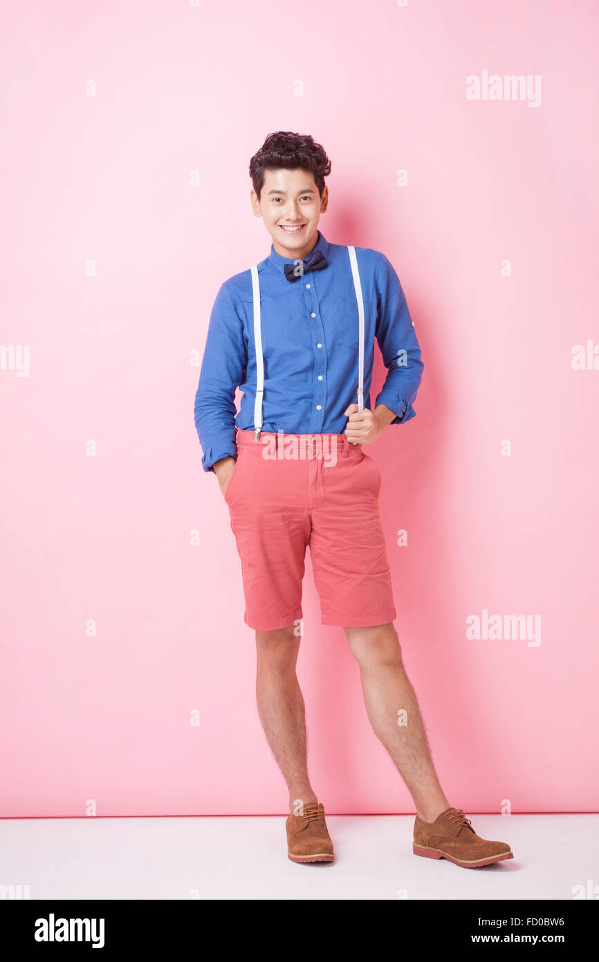 Young adult man in retro style with bow tie standing on pink background with his hand in his pocket and on her suspender Stock Photo