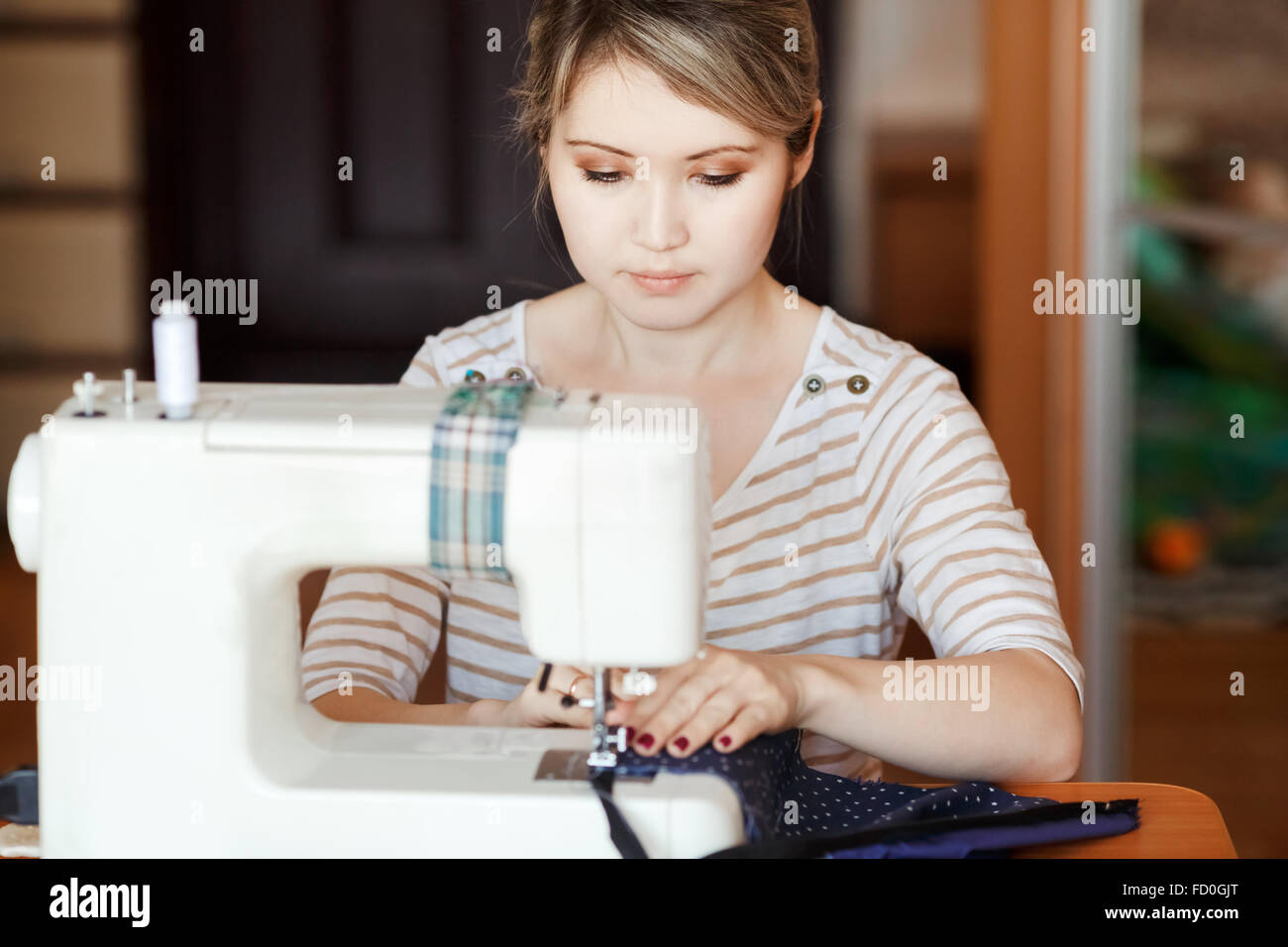 Young woman sewing with sew machine at home while sitting by her