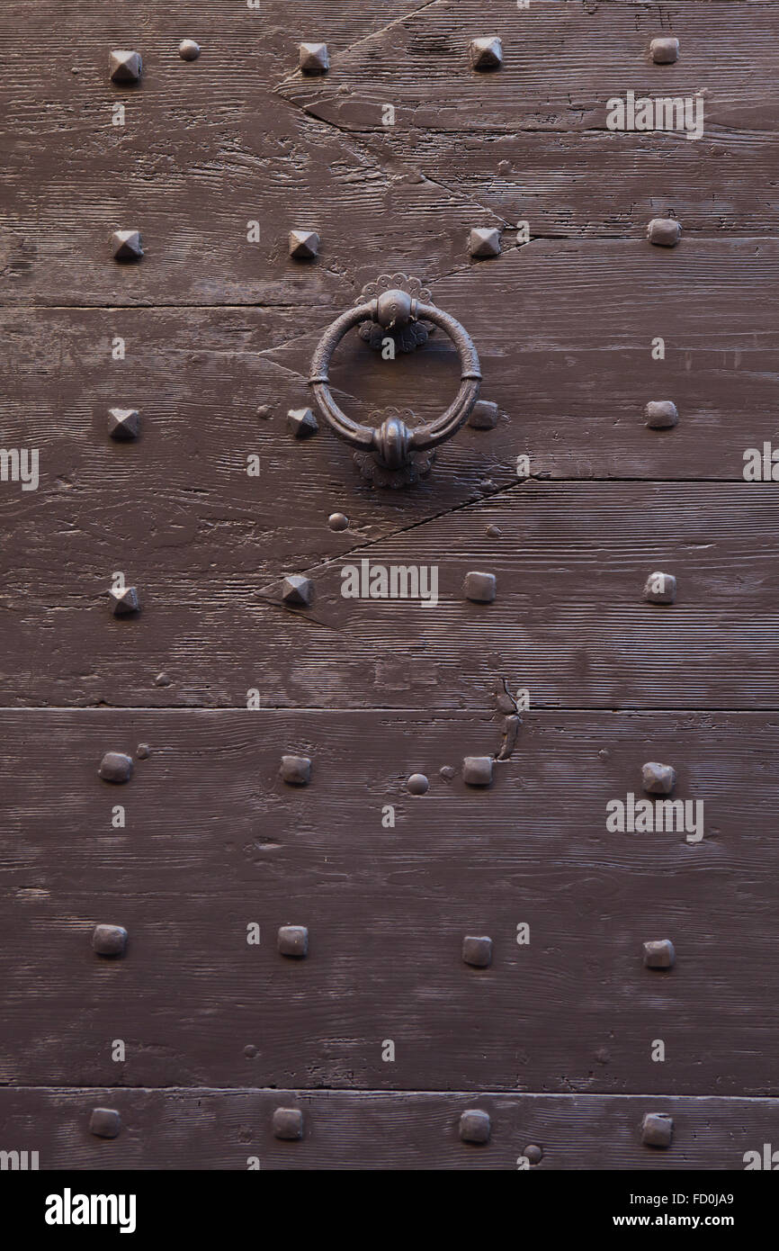 Old metal doorknocker on the brown painted wooden gate fixed with rivets in Bergamo, Lombardy, Italy. Stock Photo