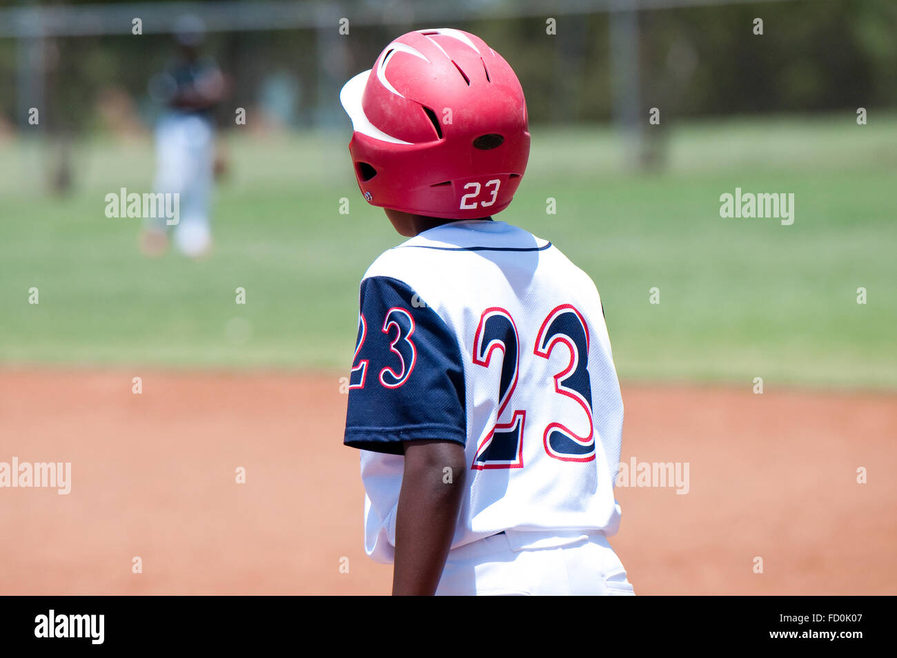 Youth baseball player wearing red helmet standing on first base. Stock Photo