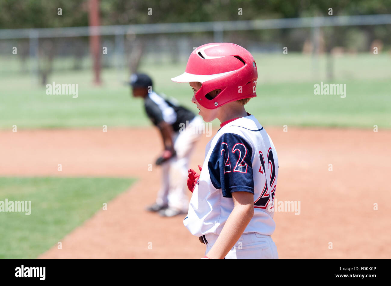 Youth baseball player wearing red helmet standing on first base. Stock Photo